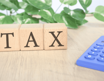 Wooden blocks spelling TAX placed on a table beside a calculator, representing income tax calculation and tax compliance TDS.