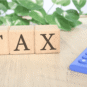 Wooden blocks spelling TAX placed on a table beside a calculator, representing income tax calculation and tax compliance TDS.