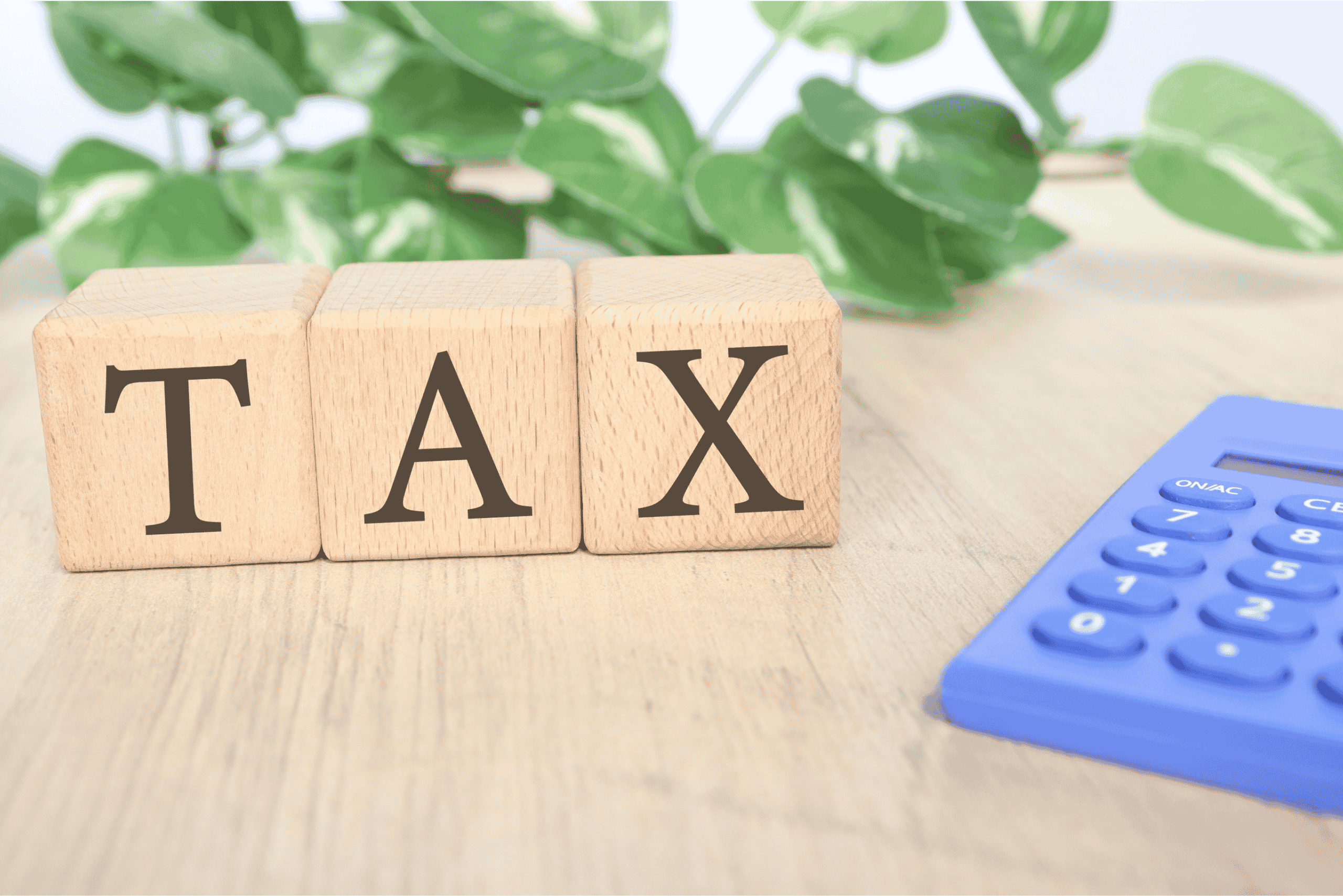 Wooden blocks spelling TAX placed on a table beside a calculator, representing income tax calculation and tax compliance TDS.
